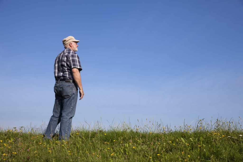 Elderly farmer standing out in green field