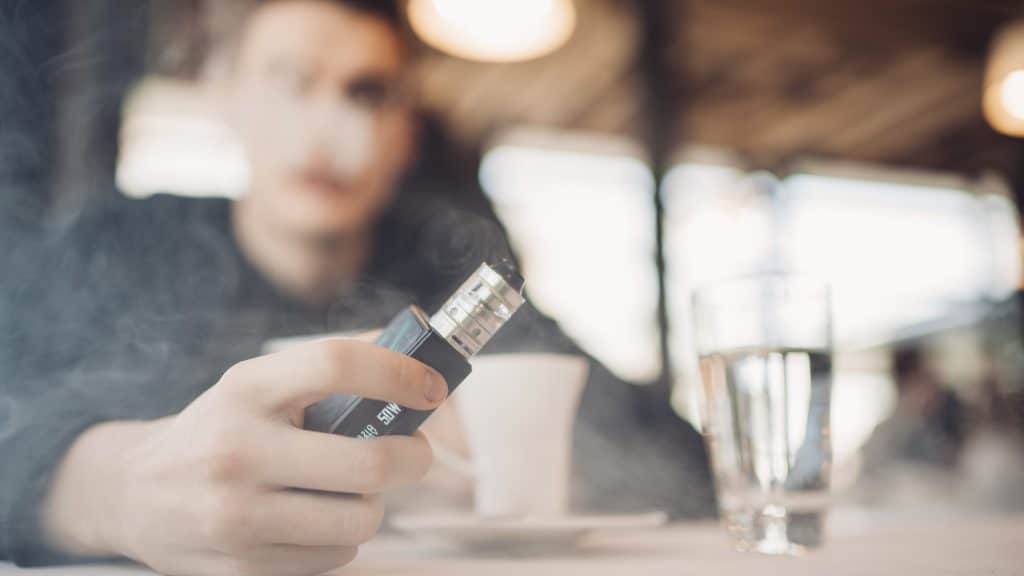 teen vaping e-cigarette at a table