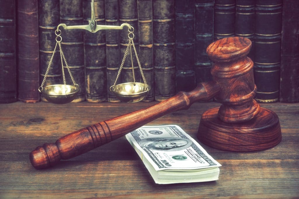 gavel sitting on table with law books, money, and scales of justice